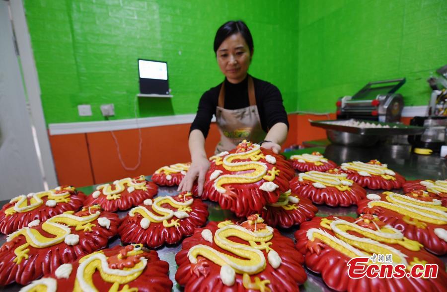 Μια γυναίκα στην πόλη Ντινγκτζόου της επαρχίας Χεμπέι δείχνει κινέζικα ψωμάκια με θέμα τον δράκο που φτιάχνονται για να καλωσορίσουν το επερχόμενο Έτος του Δράκου. (Φωτογραφία/China News Service)