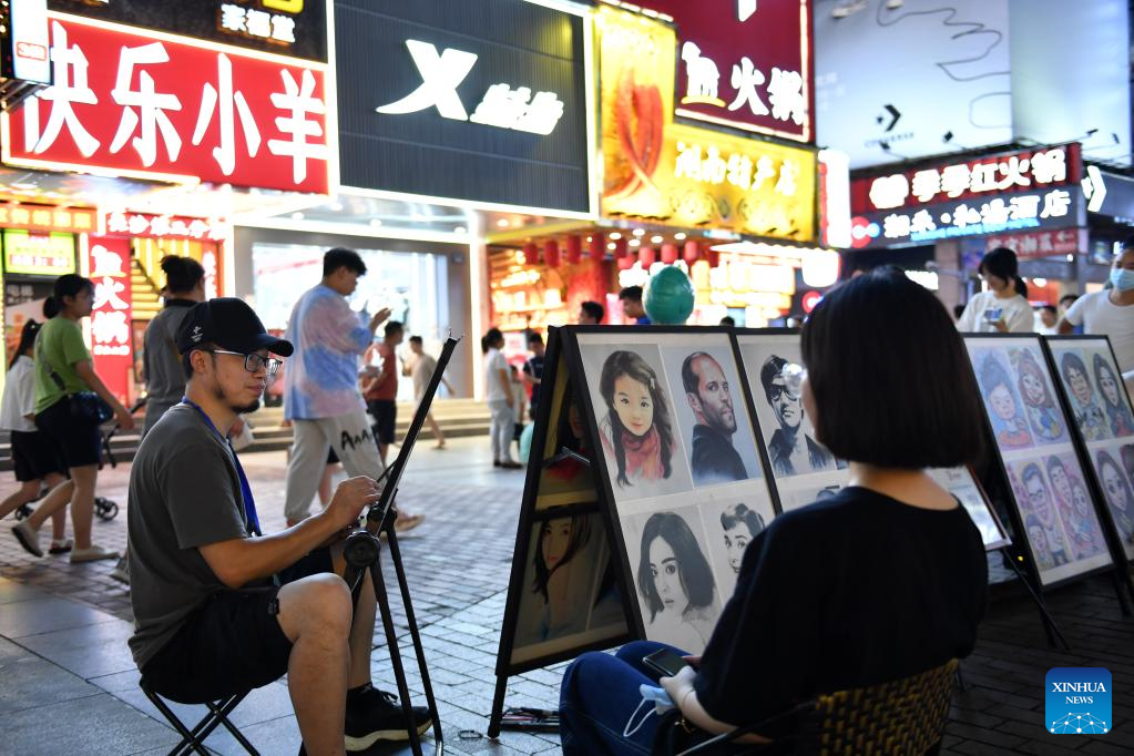 Ένας ζωγράφος (αριστερά μπροστρά) σχεδιάζει το πορτρέτο ενός τουρίστα στην οδό Χουανγκσίνγκ στην Τσανγκσά, στην επαρχία Χουνάν της κεντρικής Κίνας, 29 Ιουλίου 2022. (Xinhua/Chen Zhenhai)