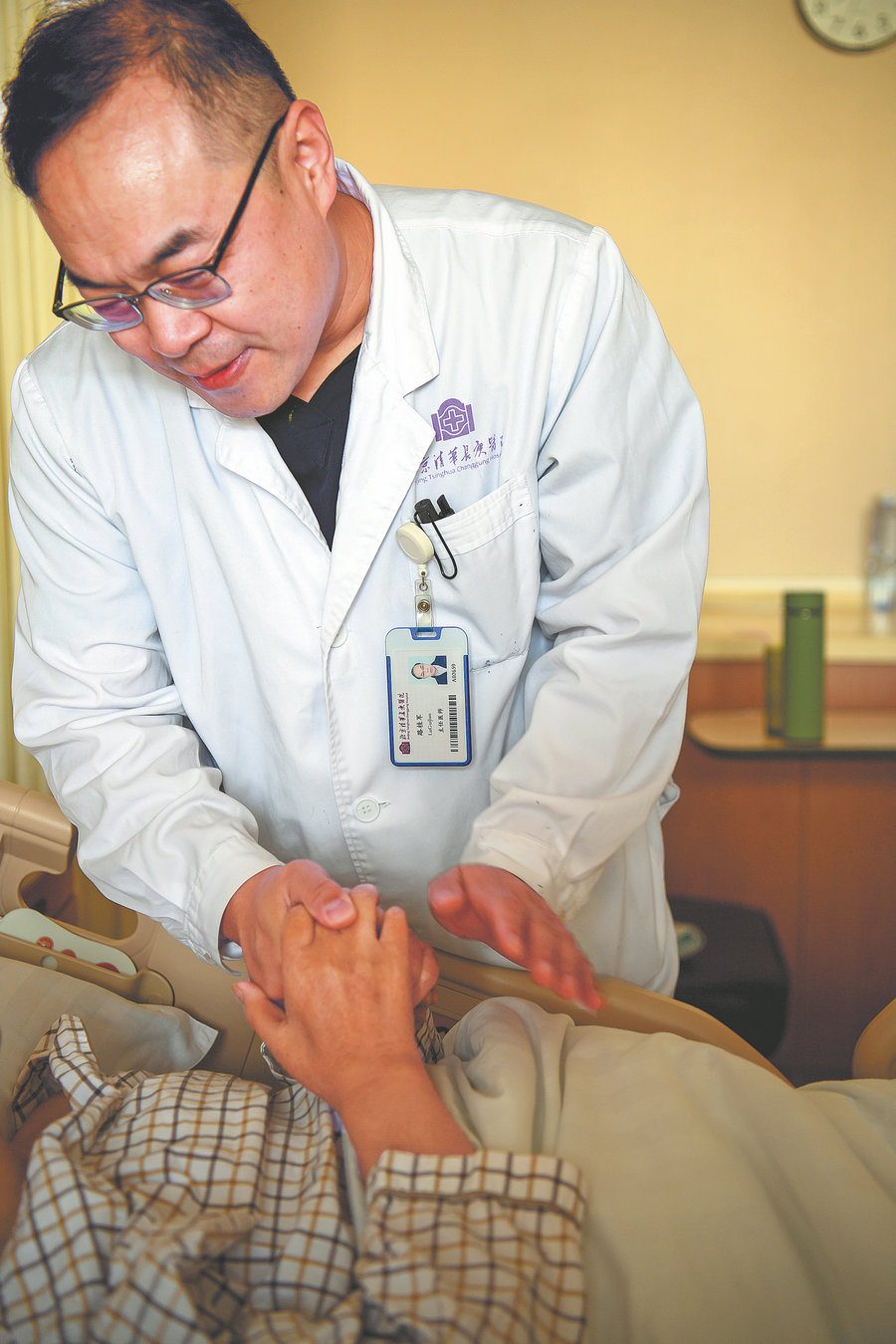 Ένας γιατρός συνομιλεί με έναν ασθενή που κρατά το χέρι του στο νοσοκομείο Τσινγκχουά Τσανγκούνγκ του Πεκίνου. [Φωτογραφία από Pan Songgang/Sun Ren/For China Daily]